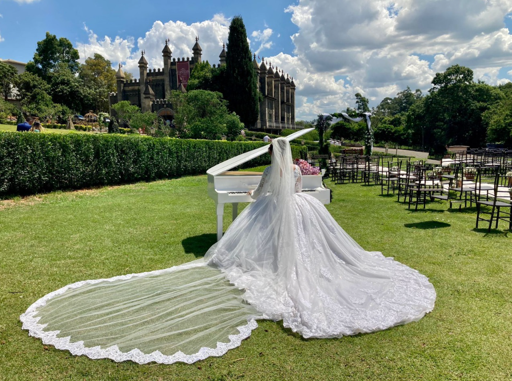 Noiva junto a um piano branco em um jardim, com arquitetura de castelo ao fundo