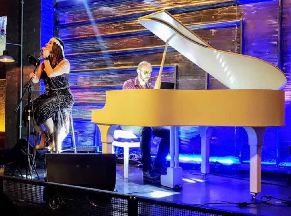 Piano branco em apresentação com músicos e iluminação de palco