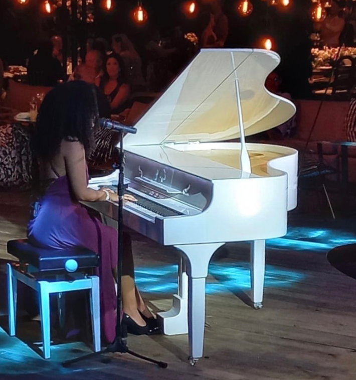 Pianista tocando um piano branco em um evento com iluminação intimista
